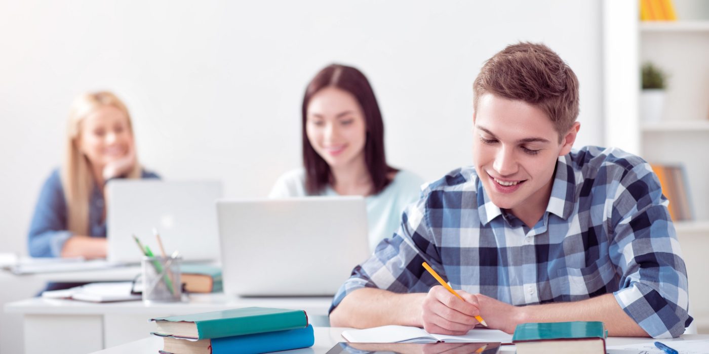 Doing my task. Group of involved and concentrated smiling students sitting at the tables and studying in the class