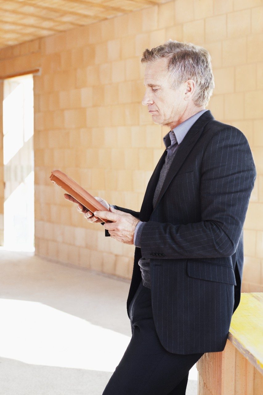 Man in suit inspecting roof tile inside unfinished building